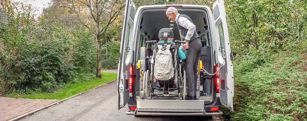 Man assisting someone in a wheelchair into car